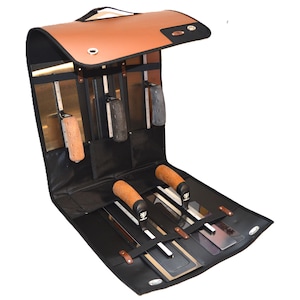 May include: Open tool roll in black and brown, featuring various trowels. The roll has a brown leather flap and handle. Several trowels with wooden and rubber handles are visible, along with metal blades. Tools are secured with straps.