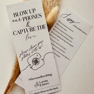 May include: Wedding cards with black text on a white background. One card reads "BLOW UP our PHONES & CAPTURE THE love." Another lists wedding moments. The cards are decorated with a camera illustration and dried plants.