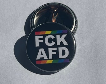 Könnte beinhalten: Ein schwarzer Knopf mit einem Regenbogenstreifen oben und dem Text "FCK AFD" in weißen Buchstaben.