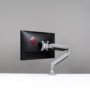 May include: A black computer monitor with a red logo is mounted on a silver and gray adjustable arm. The monitor is positioned against a gray background, with a white surface below.