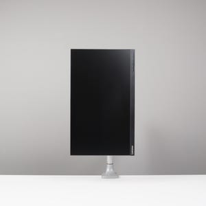 May include: A black computer monitor with a thin bezel is mounted on a silver stand. The monitor is rectangular and has a glossy screen. The stand is attached to a white surface, with a grey background.