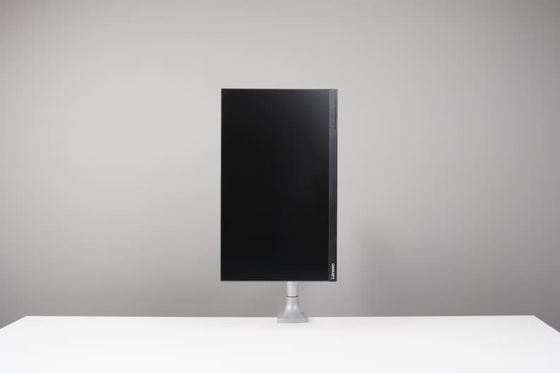 May include: A black computer monitor with a thin bezel is mounted on a silver stand. The monitor is rectangular and has a glossy screen. The stand is attached to a white surface, with a grey background.