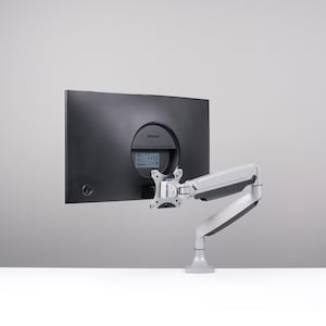 以下が含まれることがあります： 白とグレーの調整可能なアームに取り付けられた黒いコンピューターモニター。モニターの背面には「SAMSUNG」のブランド名が見える円形のくぼみがあります。アームは白いベースに取り付けられています。