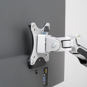 May include: A silver and black monitor arm is attached to the back of a dark grey computer monitor. The arm is designed to hold the monitor in place and allow for adjustments. The monitor has several ports.