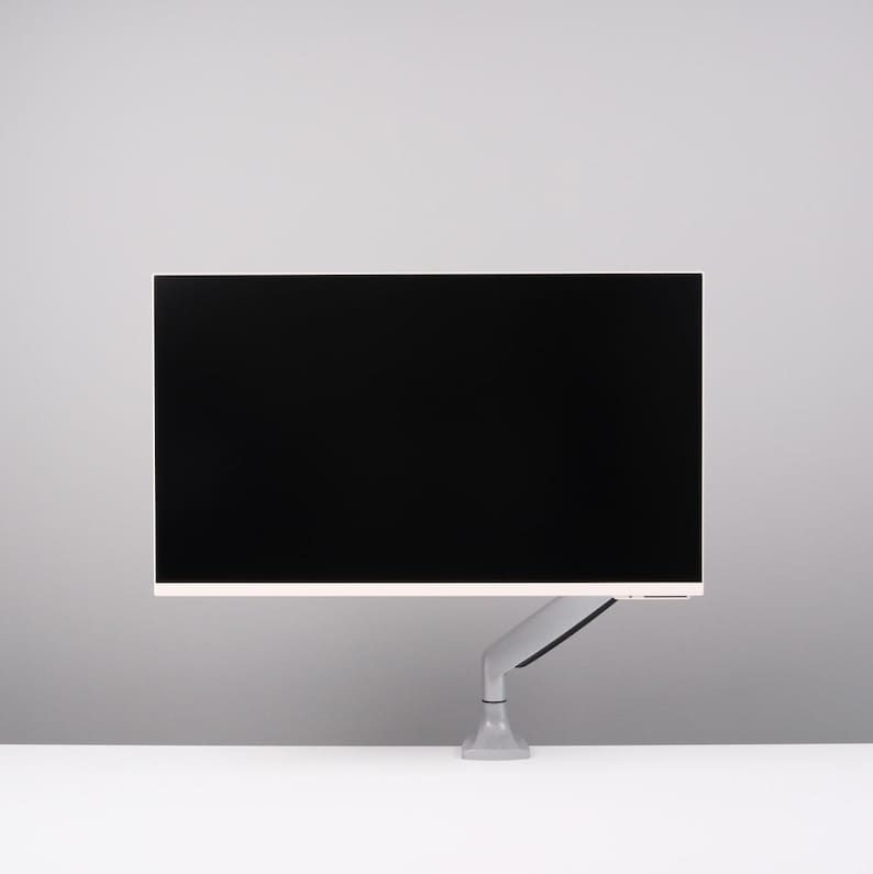 May include: A modern computer monitor with a black screen, mounted on a gray adjustable arm. The monitor has a thin white border and is set against a white and gray background. The arm is attached to a gray base.