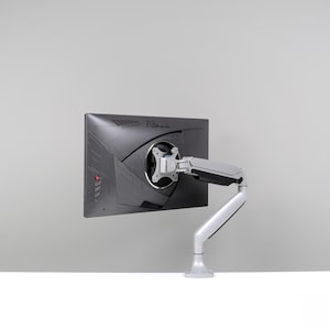 May include: A black computer monitor with the ASUS logo is mounted on a white and silver adjustable arm. The monitor is angled slightly, showcasing its back panel design. The arm is attached to a white base.