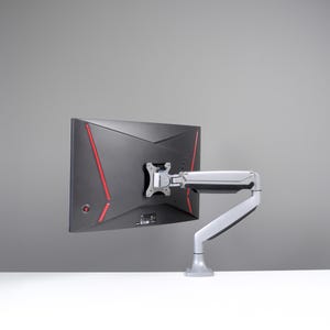 May include: A black computer monitor with red accent lines is mounted on a white and gray adjustable arm. The monitor is angled, showcasing its back panel design. The arm is attached to a white base.