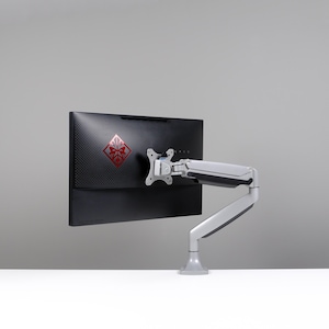 May include: A black computer monitor with a red logo is mounted on a silver and gray adjustable arm. The monitor is positioned against a light gray background, with a white surface in the foreground.