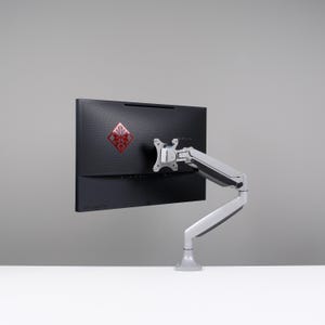 Puede incluir: Un monitor de ordenador negro con un logotipo rojo está montado en un brazo ajustable plateado. El monitor está colocado sobre un fondo gris y el brazo está fijado a una superficie blanca.