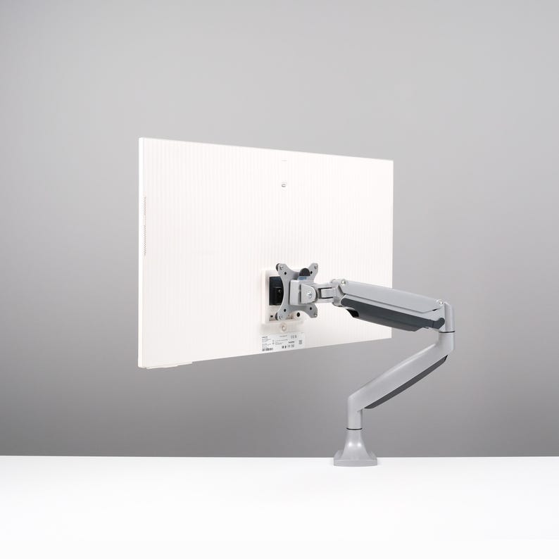 May include: A white computer monitor with a gray adjustable arm mount. The monitor is mounted on a white surface against a gray background. The arm mount allows for flexible positioning.