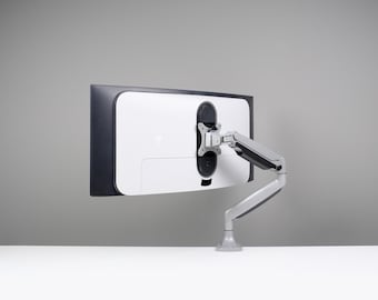 May include: A computer monitor with a white back and a black border is mounted on a gray and silver adjustable arm. The monitor is positioned against a gray background on a white surface.