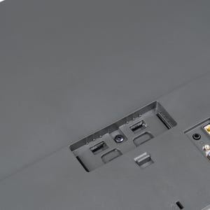 May include: Close-up of the rear of a grey computer monitor. The monitor features various ports, including USB, HDMI, and VGA. The ports are set into the monitor's casing.