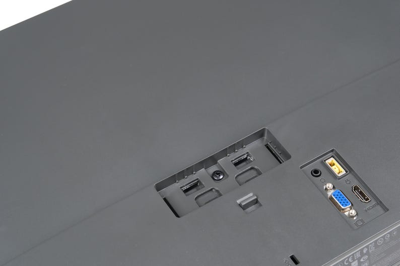 May include: Close-up of the rear of a grey computer monitor. The monitor features various ports, including USB, HDMI, and VGA. The ports are set into the monitor's casing.