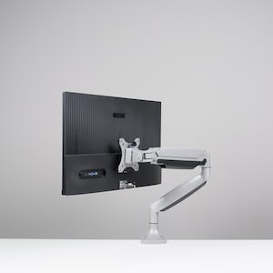 Puede incluir: Un monitor de ordenador negro montado en un brazo ajustable plateado. El monitor es rectangular con una parte trasera acanalada. El brazo está fijado a una base, lo que permite un posicionamiento flexible. La configuración está sobre una superficie blanca sobre un fondo gris.