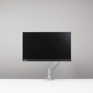 May include: A black Lenovo computer monitor mounted on a grey adjustable arm. The monitor is on a white surface against a grey background. The monitor is rectangular with a black screen.