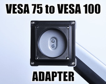 May include: Black VESA 75 to VESA 100 adapter. The adapter has four screw holes and is designed to mount a monitor or TV to a wall mount or stand.