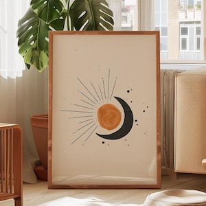 Pode incluir: Uma impressão emoldurada com um design minimalista que apresenta uma lua crescente preta e um sol amarelo com linhas radiantes. A impressão está sobre um fundo bege e é emoldurada em uma moldura de madeira marrom clara.