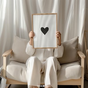 Peut inclure: Un cadre rectangulaire en bois contenant une impression blanche avec un motif de cœur noir centré. Le cadre est tenu devant le visage, le dissimulant. L'impression présente une forme de cœur noir simple et solide sur un fond blanc uni.