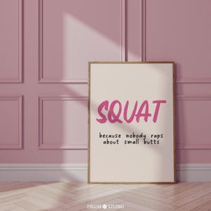 Peut inclure: Une affiche beige avec un cadre en bois rose, sur laquelle est imprimé une citation de motivation sur le fitness. La citation est "SQUAT because nobody raps about small butts".