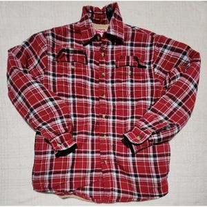 Peut inclure: Chemise à carreaux rouge, noir et blanc avec une fermeture boutonnée, deux poches de poitrine et un col. La chemise a des manches longues avec des poignets boutonnés et un col doublé de sherpa. La marque "Wrangler" est visible sur le col.