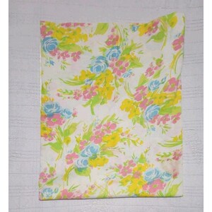 Puede incluir: Una sábana blanca con un estampado floral. El diseño presenta ramos de flores rosas, amarillas y azules con hojas verdes. Las flores están dispersas por la sábana, creando un diseño vibrante y alegre.