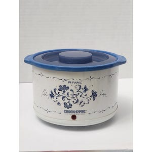 May include: A white Rival Crock-ette slow cooker with a blue lid and rim. The crock pot has a floral design in blue and the text "RIVAL" and "CROCK-ETTE" are visible.