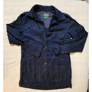 May include: A navy blue blazer with a collared neckline, two front pockets, and three buttons. The blazer has long sleeves and a relaxed fit. The brand label is visible on the inside of the collar.