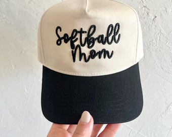 May include: A white and black baseball cap with the text "Softball Mom" embroidered in black on the front.