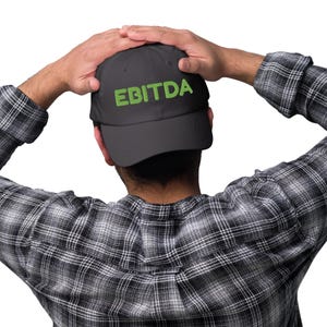 May include: A dark gray baseball cap with the word "EBITDA" in green block letters. The person in the image is wearing a black and white plaid shirt.
