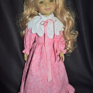 May include: A doll with long blonde hair wearing a pink dress with white floral print and a white crocheted collar with a pink ribbon.