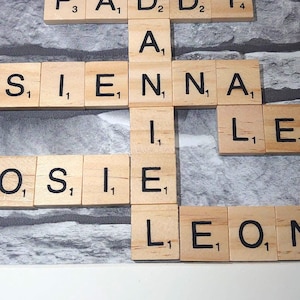 May include: A framed piece of art with the word "love" written in cursive at the top. The art is made up of Scrabble tiles spelling out the names "Paddy", "Sienna", "Leo", "Rosie", and "Leon".