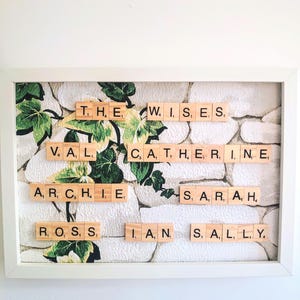 May include: A white frame with a green and white floral pattern background. The frame contains a collection of names spelled out using letter tiles. The names are: The, Wise, Val, Catherine, Archie, Sarah, Ross, Ian, and Sally.