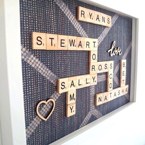 Elegante marco de fotos de Scrabble personalizado con fichas de madera con el nombre de la familia y corazones hechos a mano sobre un fondo artístico oscuro y bronce.