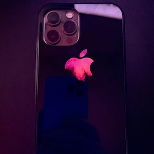 May include: A black iPhone with a red apple logo on the back. The phone has a triple camera system with three lenses.