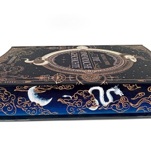 Könnte beinhalten: Ein schwarzes Hardcover-Buch mit einem goldenen und weißen Design. Der Titel des Buches lautet "Die Unendliche Geschichte" und der Autor ist Michael Ende. Das Buch ist geschlossen und der Rücken ist zur Kamera gerichtet.