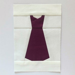 May include: A white fabric square with a burgundy fabric dress shape cut out of the center.