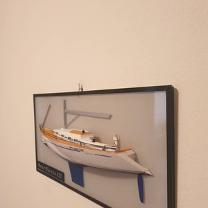 Könnte beinhalten: Ein gerahmtes Modell eines weißen Segelboots mit blauen Akzenten. Das Modell trägt den Titel "Relax Bavaria 430" und die Registrierungsnummer "BC 3092 DX" an der Seite.