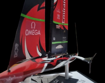 May include: A red and black model sailboat with the words "Emirates Fly Better" on the sail. The sailboat is on a black base with a compass design and the words "Te Rehutai 36 America's Cup Auckland 2021".
