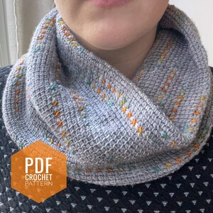 May include: A gray crochet cowl with colorful accents. The cowl is folded and worn around a person's neck. The text "PDF CROCHET PATTERN" is on a orange hexagon.