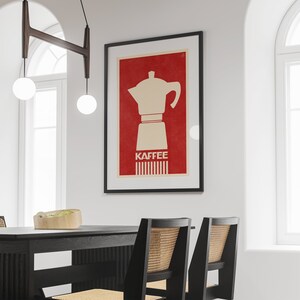 Pu&ograve; includere: Un poster incorniciato con sfondo rosso e una silhouette bianca di una caffettiera. Il testo "Kaffee" &egrave; stampato in bianco sotto la caffettiera.
