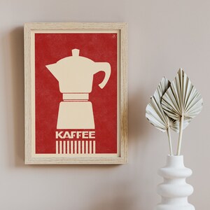 Pu&ograve; includere: Una stampa incorniciata con sfondo rosso e una silhouette bianca di una caffettiera. Il testo "Kaffee" &egrave; stampato in bianco sotto la caffettiera.