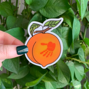 May include: A peach sticker with a handprint on it. The peach is orange and the handprint is red.