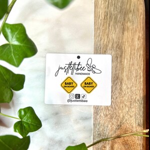 May include: Two yellow "Baby on Board" signs with black text on a white card with the text "justlettiibee HANDMADE" and social media icons.