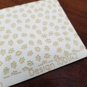May include: A white sheet of paper with a repeating pattern of paw prints. The text "Design 100142" is printed on the bottom right corner of the paper.