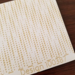May include: A white card with a pattern of small, raised, gold circles. The text "Design 100387" is printed in gold at the bottom right corner.