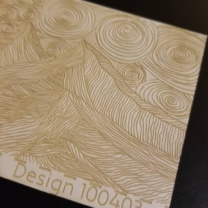 May include: A close-up of a laser-cut wooden design with a swirling pattern. The design is labeled "Design 100403".