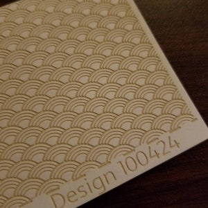 May include: A close-up of a white textured surface with a repeating pattern of overlapping semicircles. The text "Design 100424" is printed in the bottom right corner.