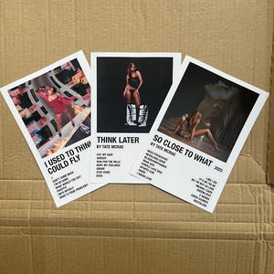 May include: Three white rectangular prints featuring album art and song titles by Tate McRae. The prints are titled "I Used To Think I Could Fly", "Think Later", and "So Close To What". The prints are on a brown cardboard surface.
