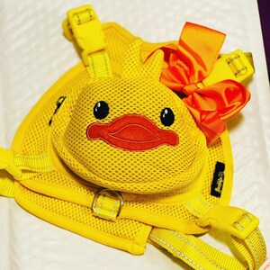 Puede incluir: Arn&eacute;s de perro de malla amarilla con una pieza de pecho en forma de pato y un lazo rojo. El arn&eacute;s tiene una hebilla amarilla y un anillo amarillo para sujetar una correa.