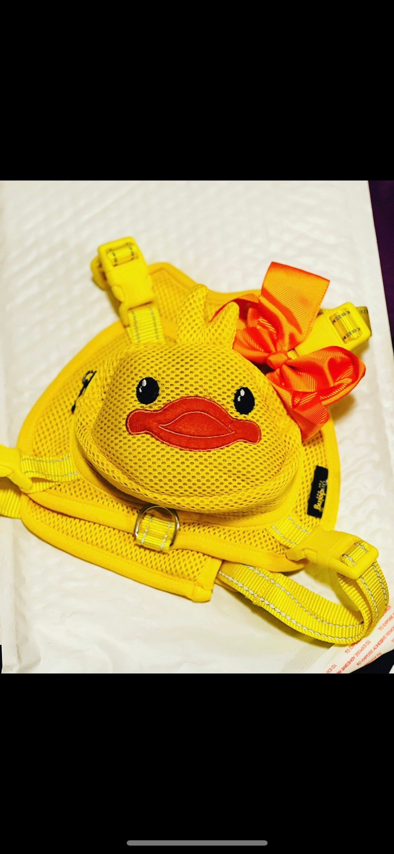 Puede incluir: Arn&eacute;s de perro de malla amarilla con una pieza de pecho en forma de pato y un lazo rojo. El arn&eacute;s tiene una hebilla amarilla y un anillo amarillo para sujetar una correa.